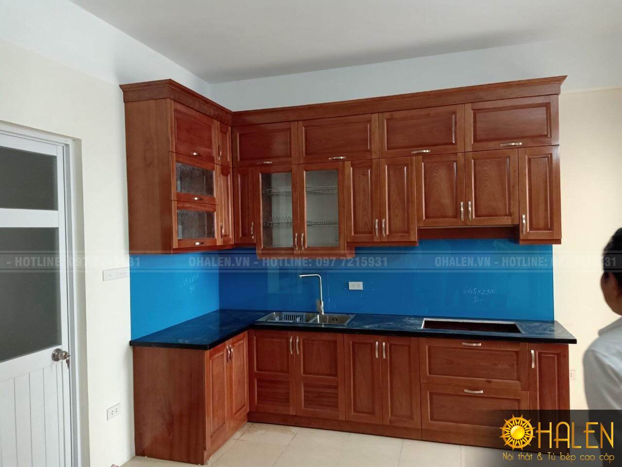 Tủ bếp gỗ xoan đào phun màu cánh gián ấm cúng với điểm nhấn là kính bếp màu xanh dương